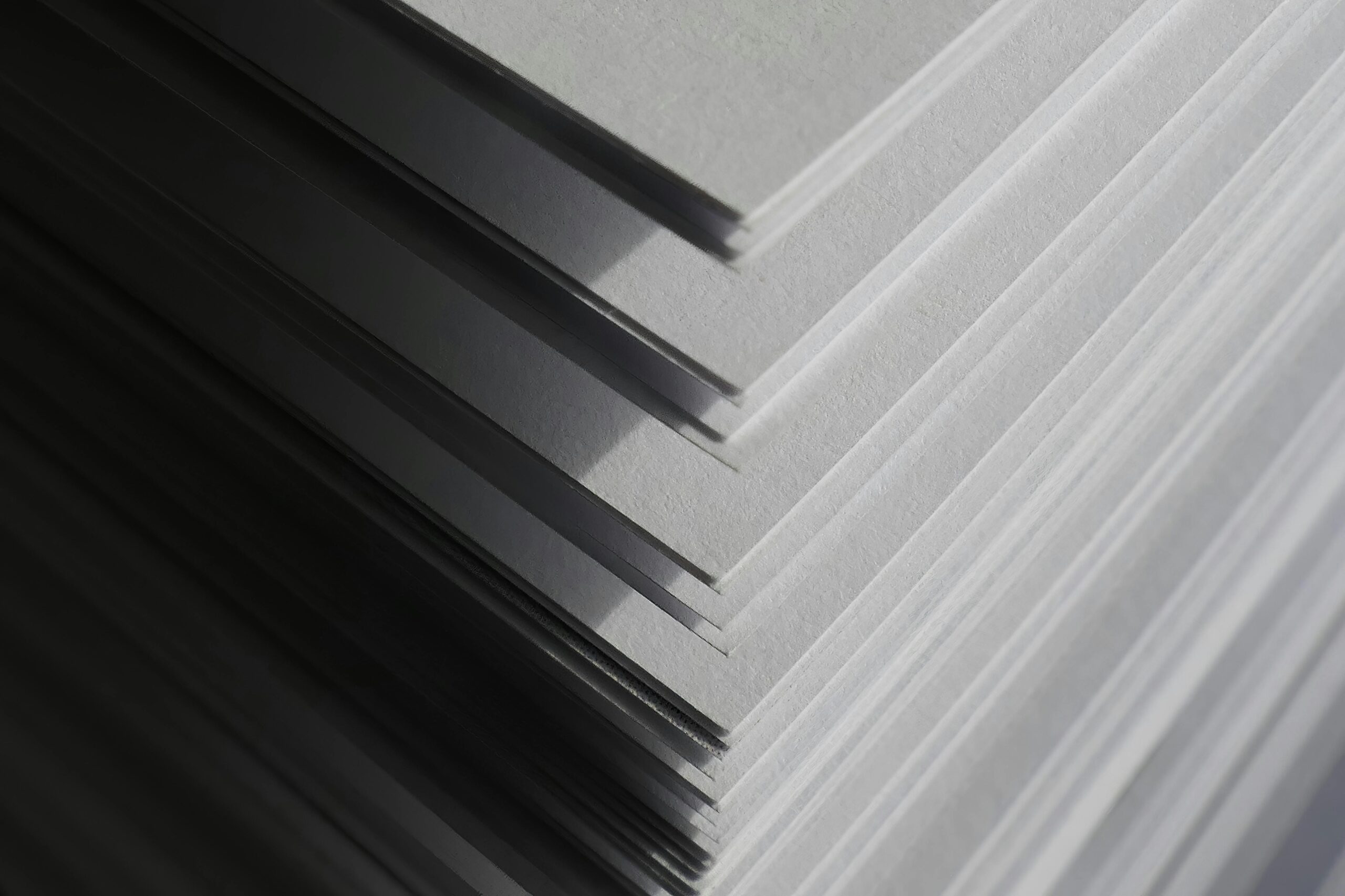 Artistic close-up of stacked white paper sheets creating geometric shadows and patterns in soft light.